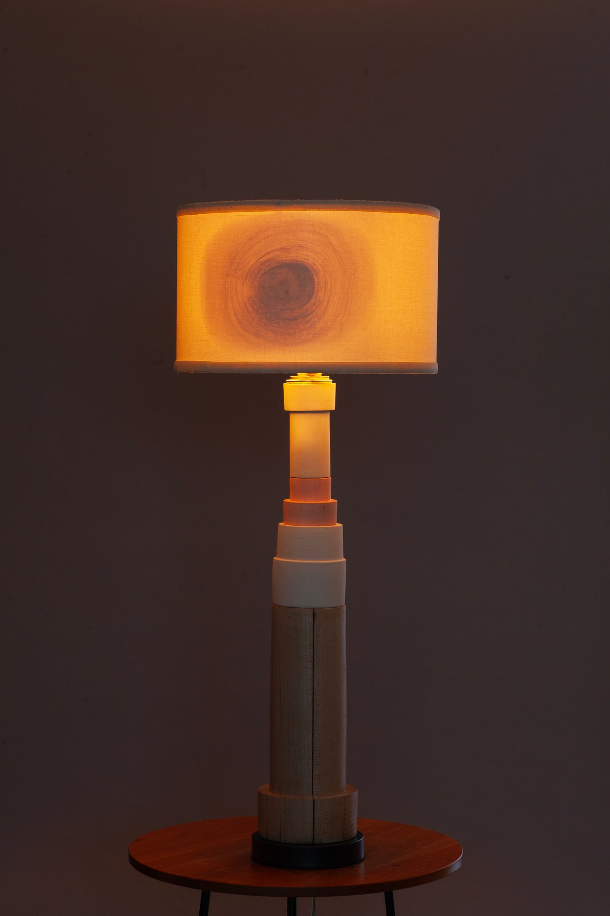 A modern table lamp with a cylindrical light-activated base and a rectangular drum shade, glowing with warm amber light against a dark background.